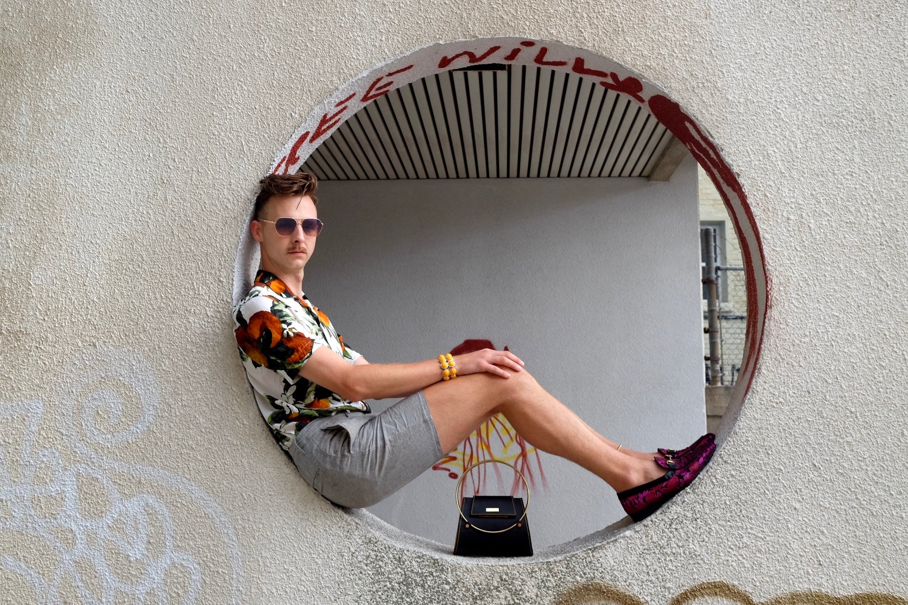 Young man sits in circular opening showcasing leather purse  