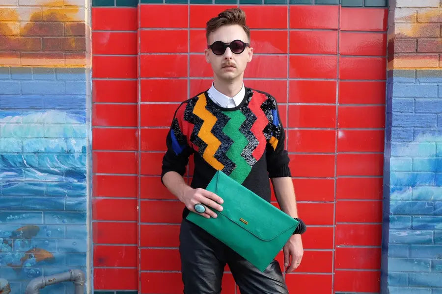Man in 80’s sparkly sweater holds green leather clutch  