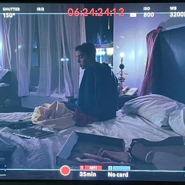 Screenshot of a camera viewfinder. Woman sits on bed. 