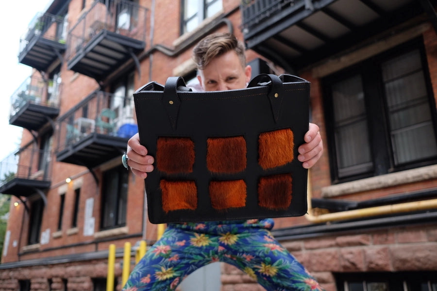 Man holds black tote bag towards camera. 