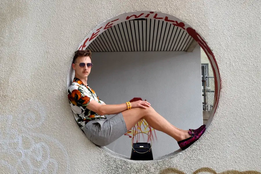 Man sits in large circle opening in wall displaying small black purse 